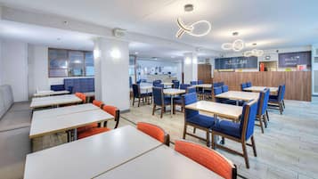 A modern restaurant with multiple tables and booths, a counter area, and a visible menu board.
