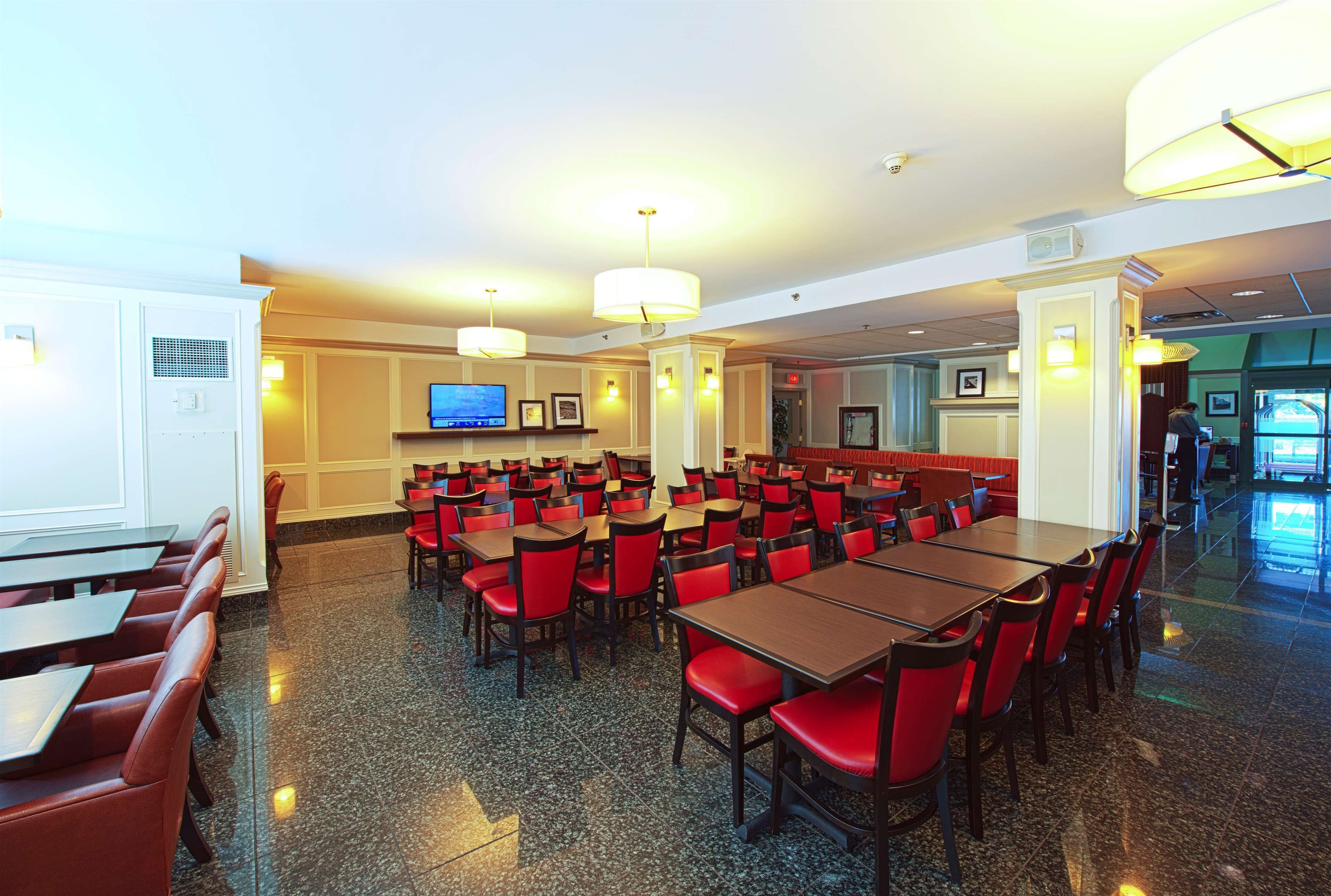 A spacious dining area with multiple tables and chairs, a television mounted on the wall, and a clean, polished floor.
