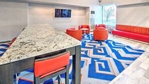 Un hall d’hôtel moderne avec un comptoir d’accueil en marbre, des sièges rouges et une moquette à motifs.