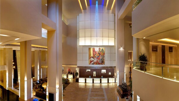 A spacious lobby with a reception desk, seating areas, and a large artwork on the wall. - The LaLiT New Delhi (New Delhi)