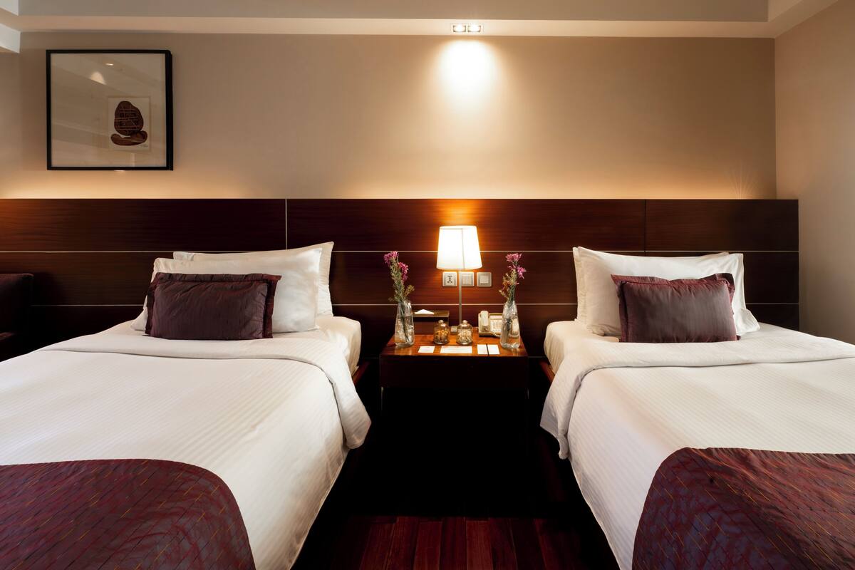 Ein Hotelzimmer mit zwei Betten, einem Nachttisch mit Lampe und einem gerahmten Bild an der Wand.