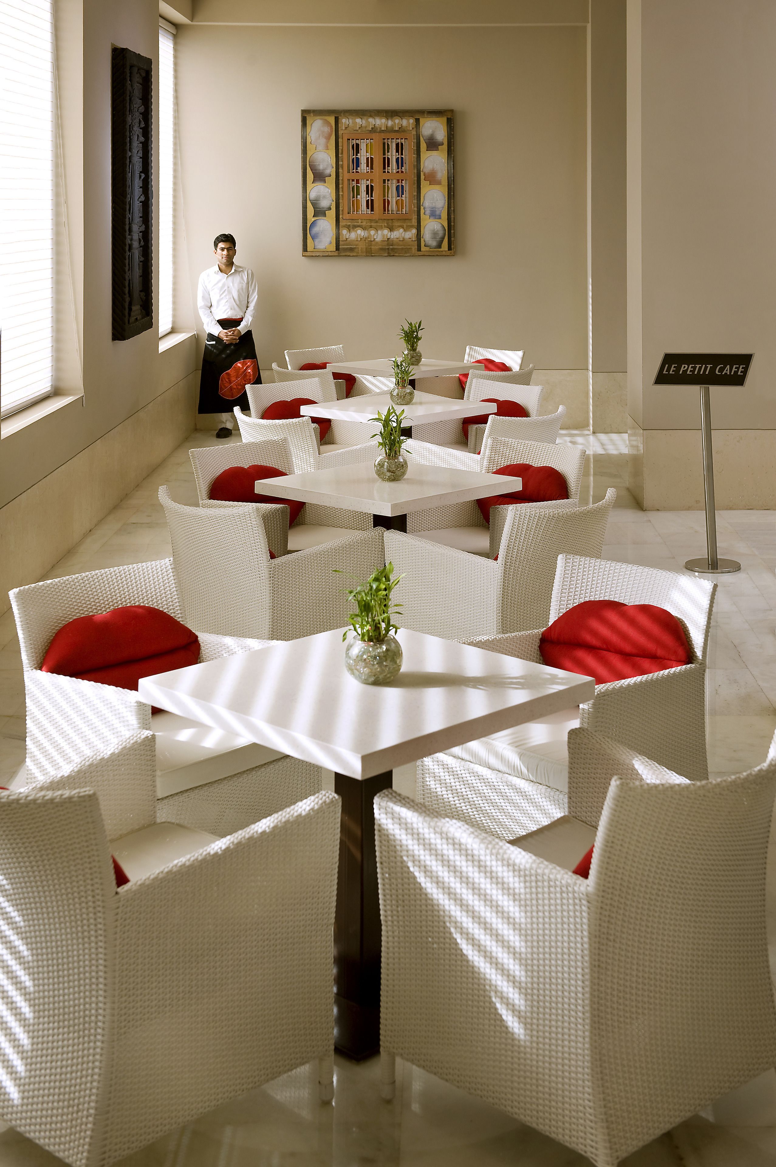 Uma sala de jantar com móveis de vime branco, almofadas vermelhas e pequenos vasos com plantas.