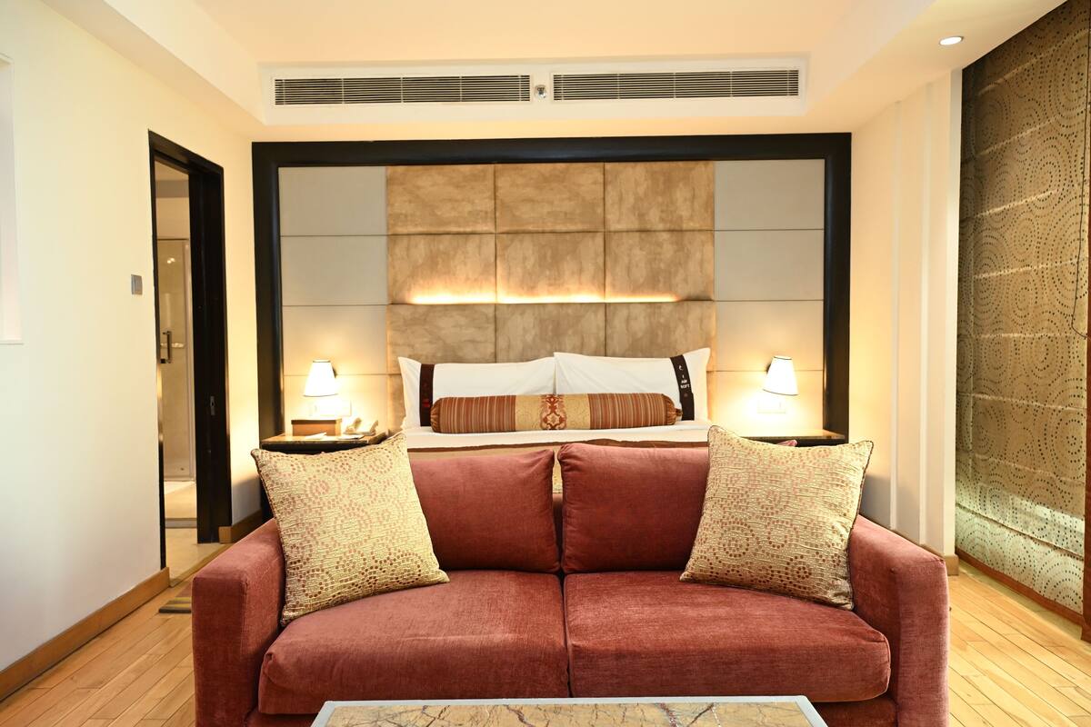 Ein modernes Hotelzimmer mit einem großen Bett, zwei Nachttischlampen, einem roten Sofa und einer Wand mit Muster.