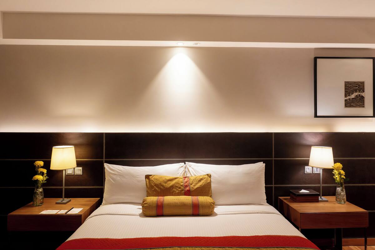 Ein Hotelzimmer mit einem ordentlich bezogenen Bett, zwei Nachttischen mit Lampen und einem gerahmten Bild an der Wand.