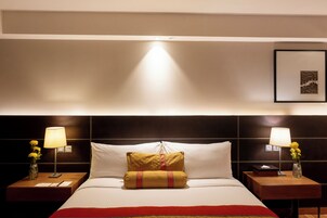 Una habitación de hotel con una cama bien hecha, dos mesitas de noche con lámparas y un cuadro en la pared.