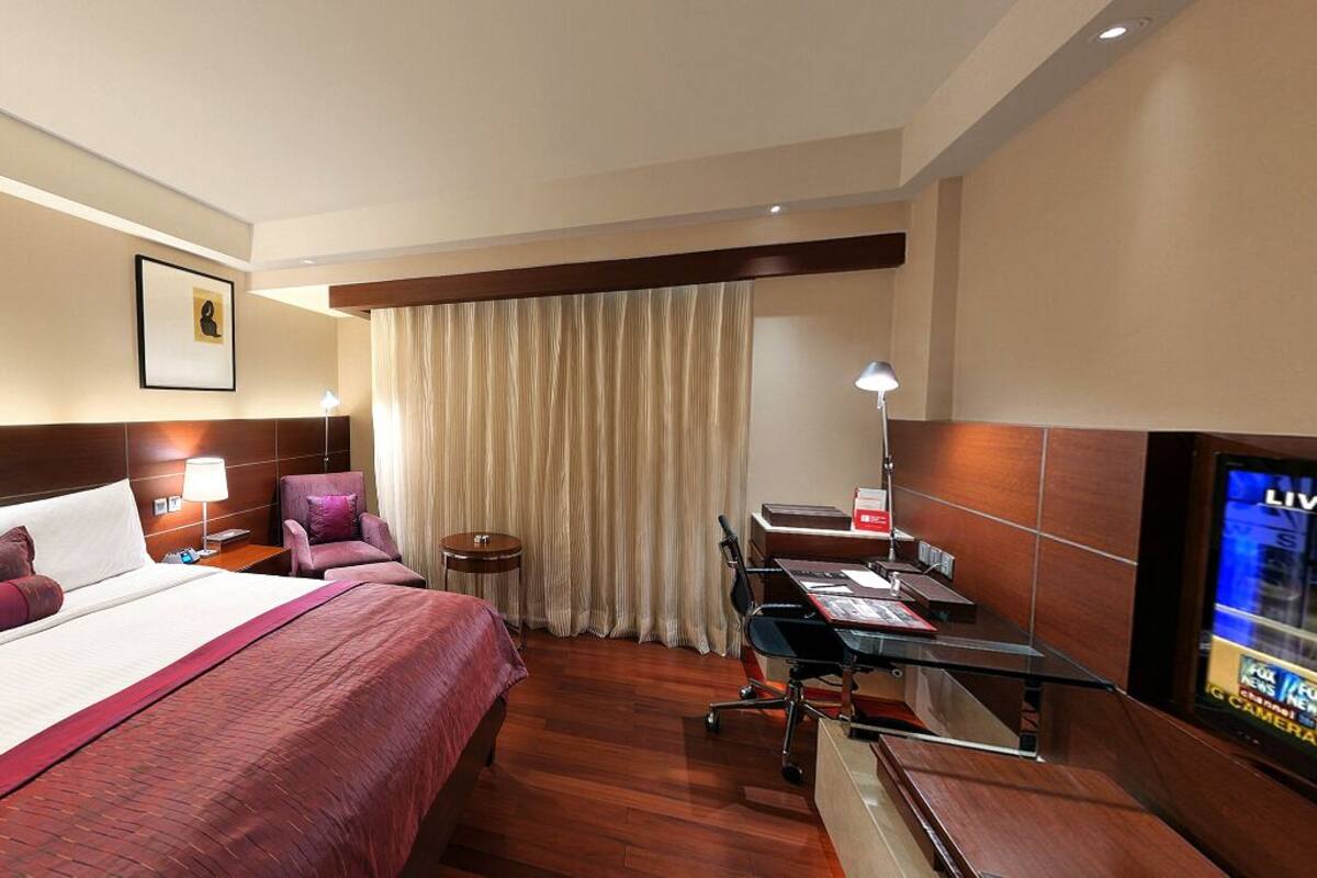 Ein Hotelzimmer mit einem großen Bett, einem Schreibtisch mit Computer, einem Fernseher und einem Sessel.