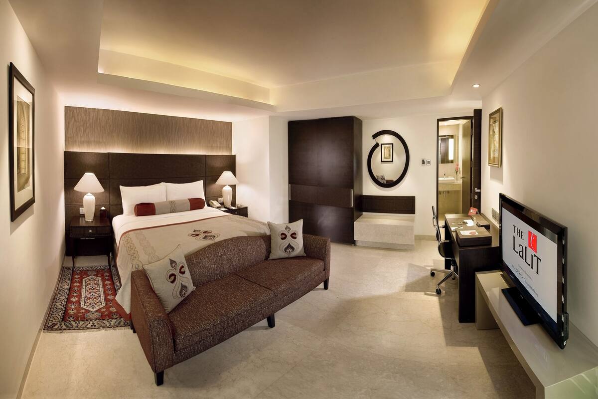 Ein modernes Hotelzimmer mit einem großen Bett, einer Couch, einem Schreibtisch mit Fernseher und einem durch eine offene Tür einsehbaren Badezimmer.