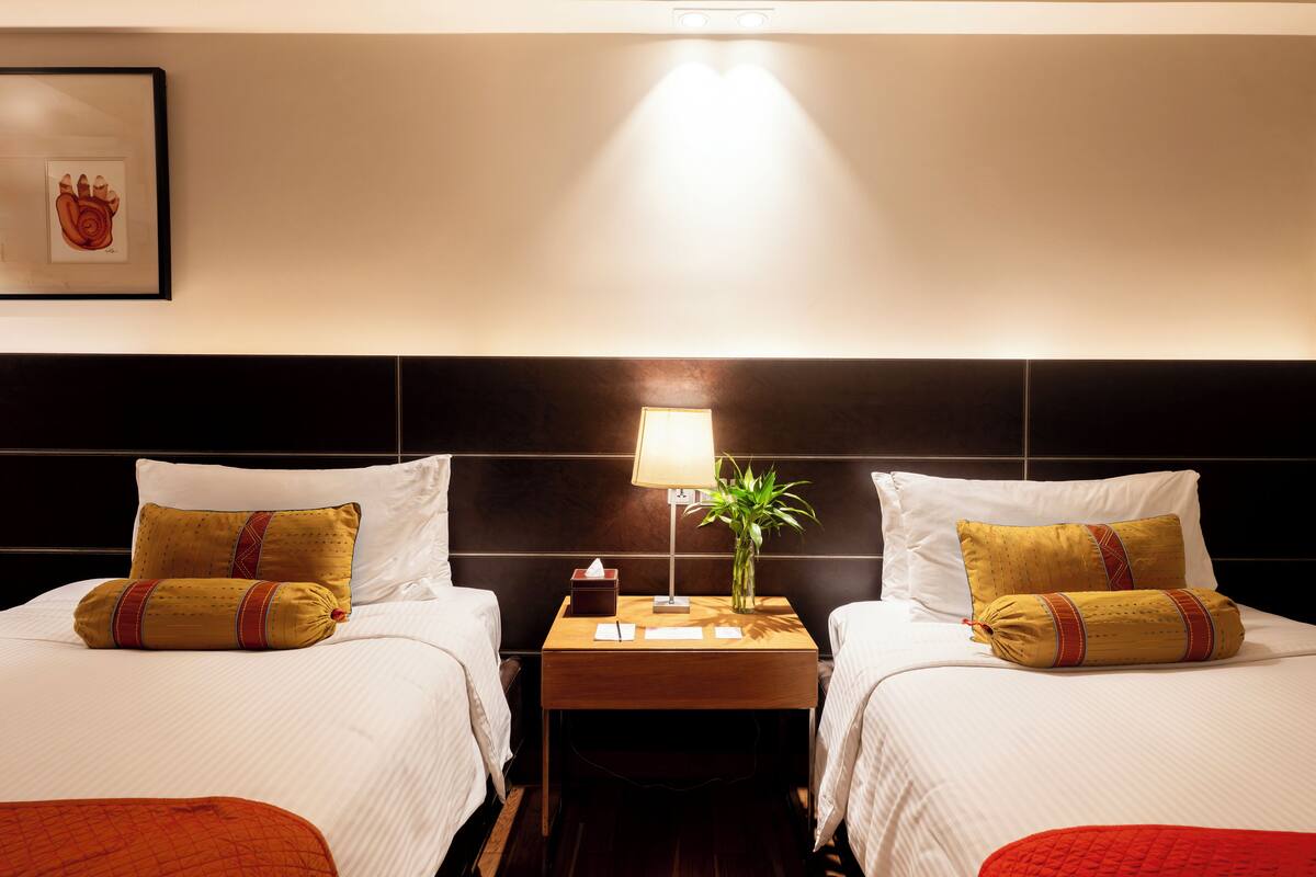 Ein Hotelzimmer mit zwei Betten, einem Nachttisch mit Lampe und Blumenvase sowie einem gerahmten Bild an der Wand.