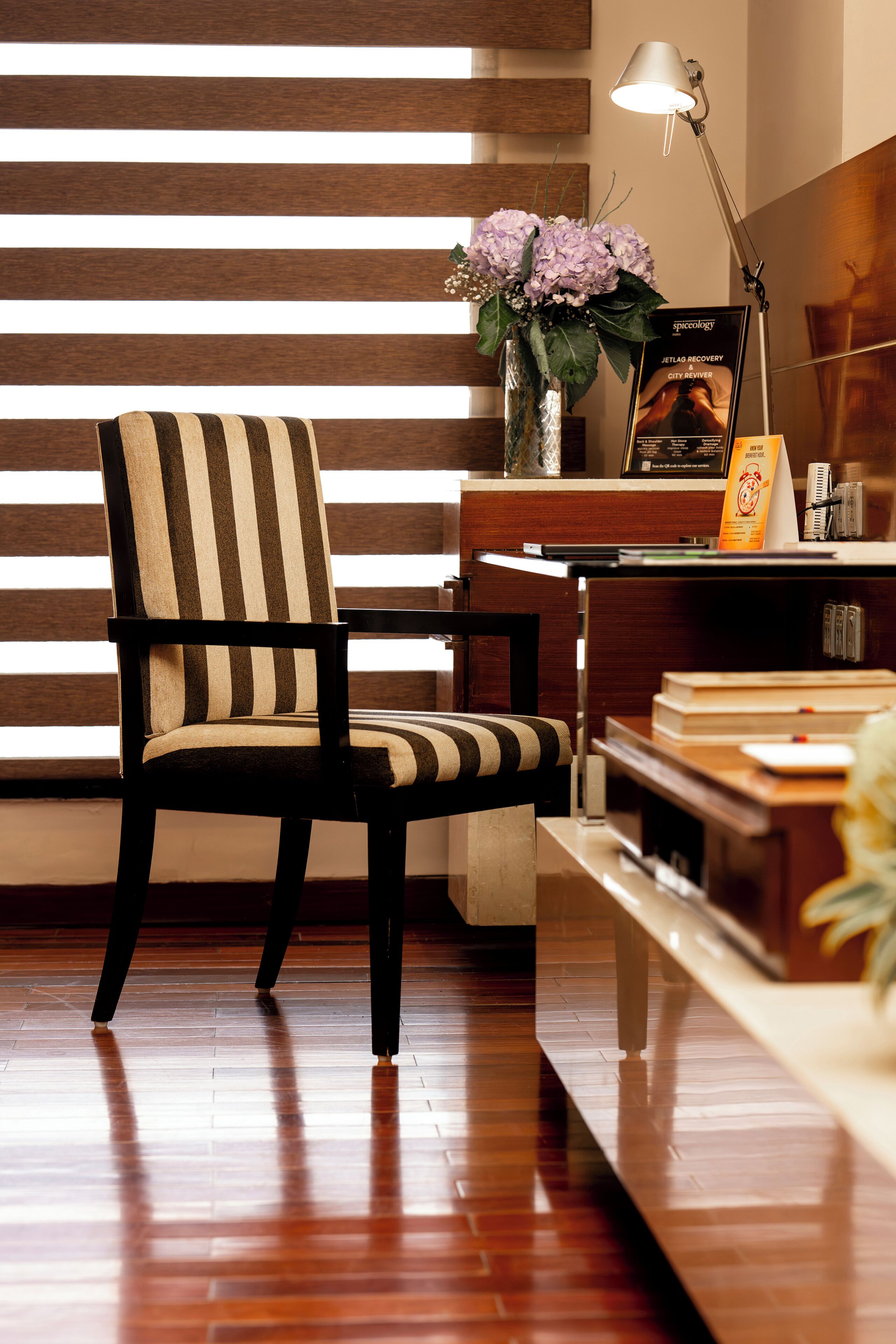 A striped chair, a desk, a lamp, and a poster in a room with wooden flooring and a striped wall.