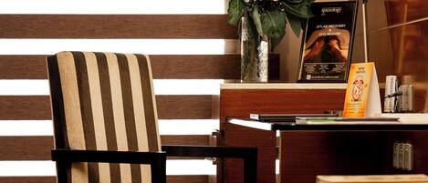 A striped chair, a desk, a lamp, and a poster in a room with wooden flooring and a striped wall.