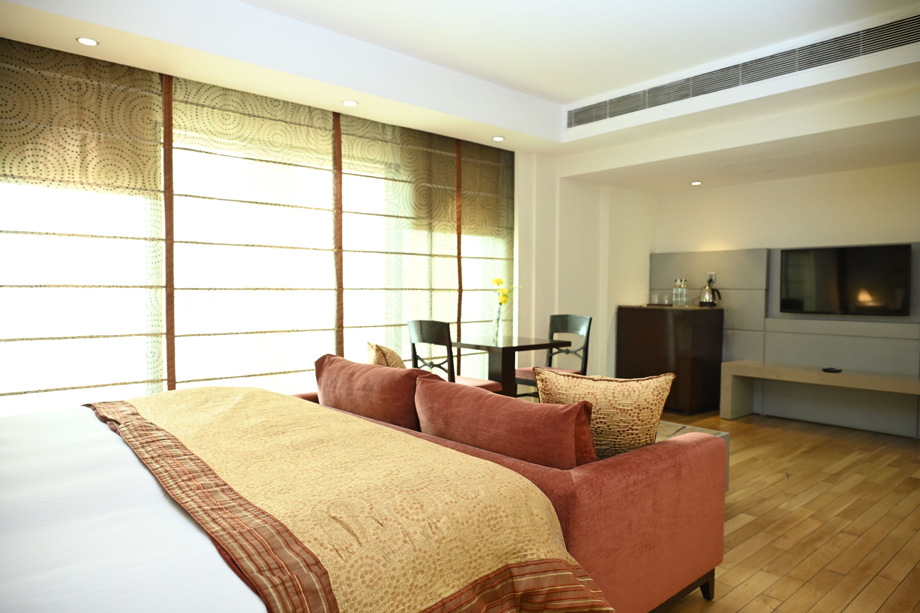 A modern hotel room with a large bed, a sofa, a TV, and a dining area.