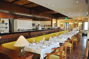 Un ristorante con lunghe tavole, comode panche imbottite di giallo e uno chef ai fornelli.