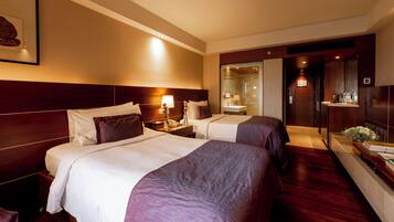 A hotel room with two beds, a nightstand, a lamp, a mirror, and a bathroom visible through a glass door.