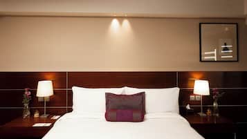 A hotel room with a neatly made bed, two bedside tables with lamps, a nightstand with a vase and a small decorative item, and a framed picture on the wall.