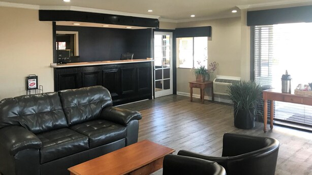A living room with a black leather sofa, a wooden coffee table, and black armchairs. There is a black entertainment unit with a TV and speakers, and a potted plant near a window. - Rodeway Inn Ontario Airport Mills (Ontario)
