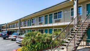 A multi-story motel with a parking lot, outdoor plants, and a staircase leading to the entrance. - Rodeway Inn Ontario Airport Mills (Ontario)