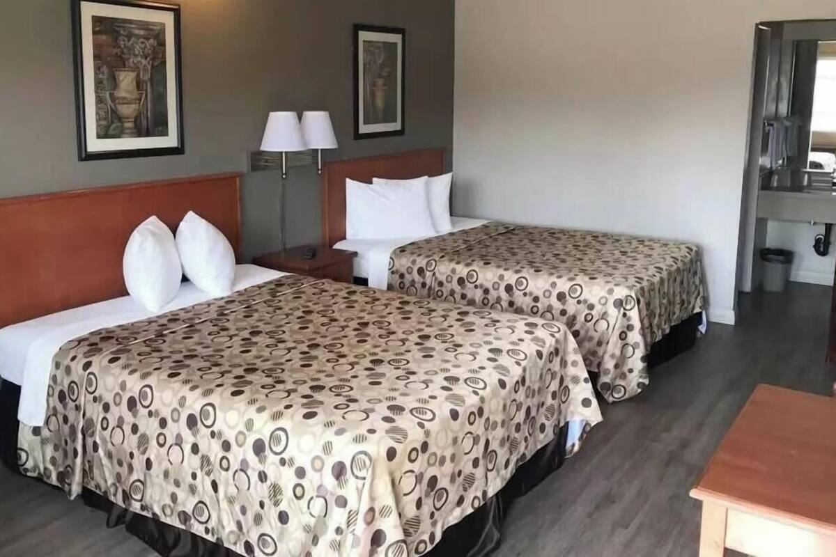 A hotel room with two beds, a wooden headboard, a nightstand, a lamp, and a framed picture on the wall.