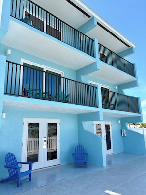 A two-story building with balconies, a covered entryway, and a concrete patio with two Adirondack chairs. - The Bay Inn at Lani Kai (Fort Myers Beach)