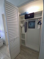 A walk-in closet with a sliding door, shelves, a hanging rod, and a microwave.