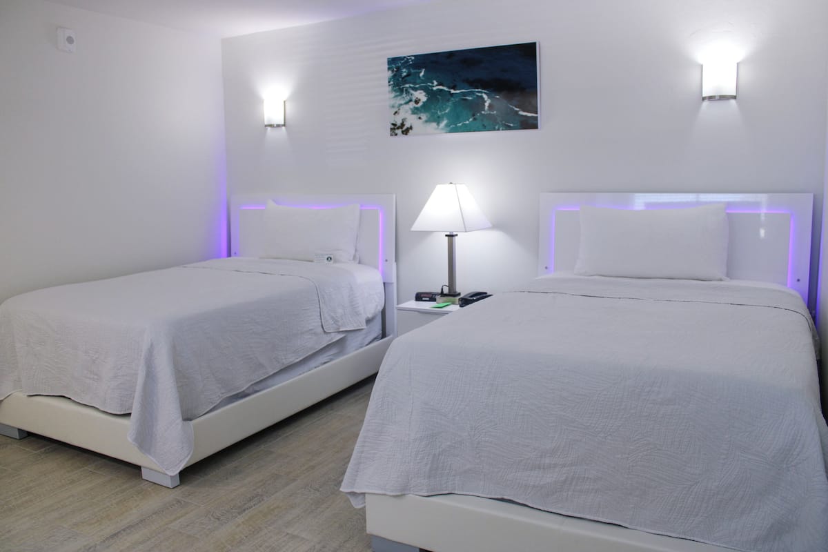 Two single beds with white bedding, a nightstand with a lamp, and a wall-mounted painting.