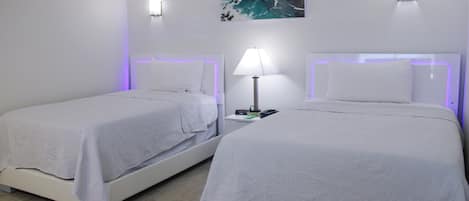 Two single beds with white bedding, a nightstand with a lamp, and a wall-mounted painting.