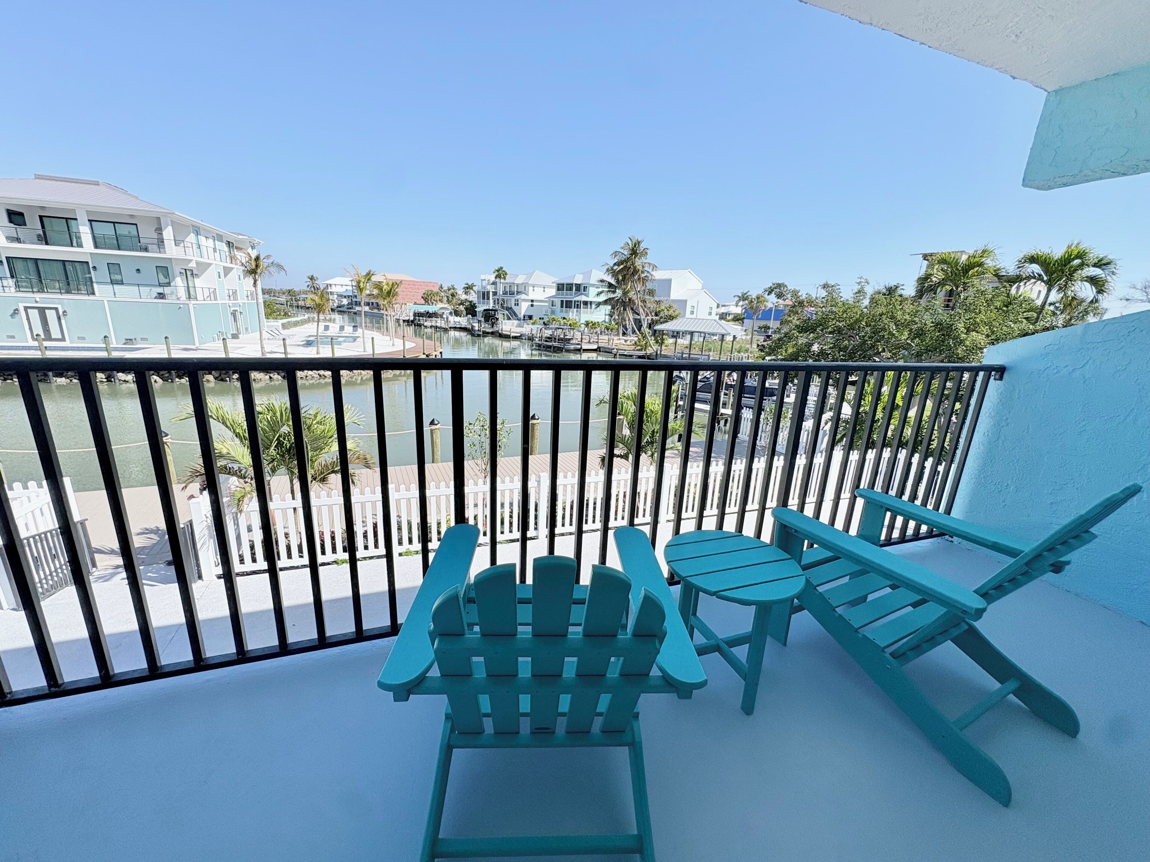 Un balcon avec deux chaises et une petite table, donnant sur une marina où l’on peut admirer des bateaux et des bâtiments.