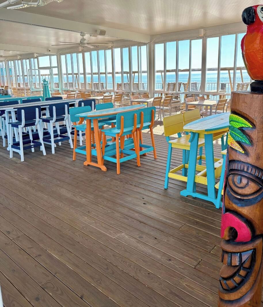 A deck area with multiple tables and chairs, large windows, and a view of the ocean.