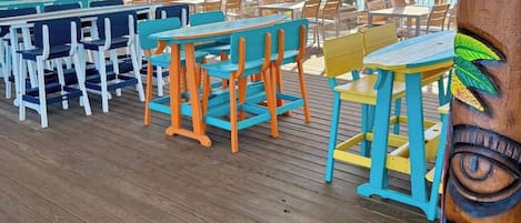 A deck area with multiple tables and chairs, large windows, and a view of the ocean.