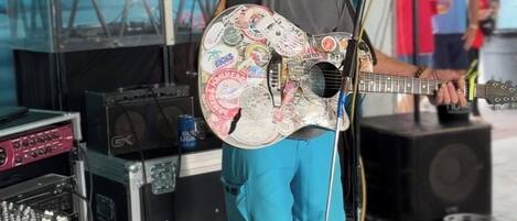 A person playing a guitar with a microphone stand in a room with sound equipment and a turtle mural on the wall.