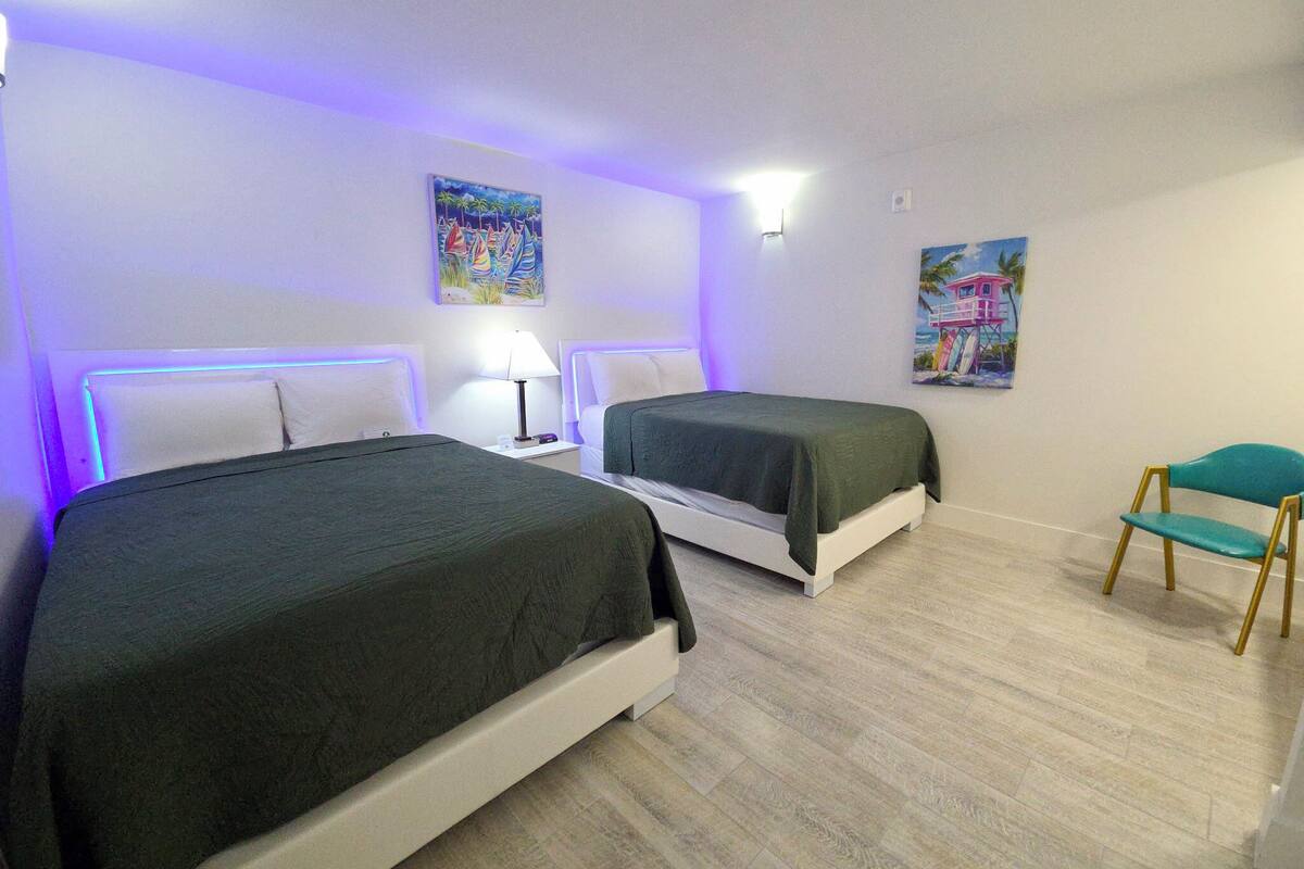A hotel room with two beds, a chair, and artwork on the walls.