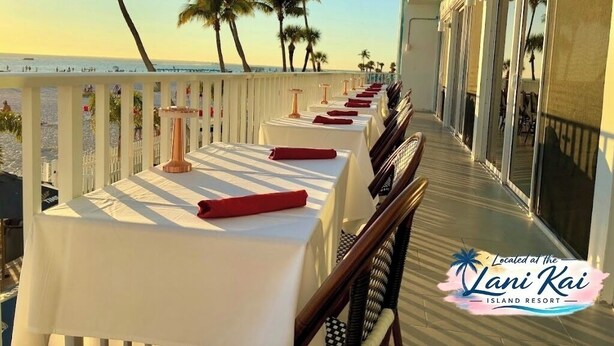 Un balcon avec des tables dressées pour le dîner, donnant sur une plage bordée de palmiers et sur l’océan.