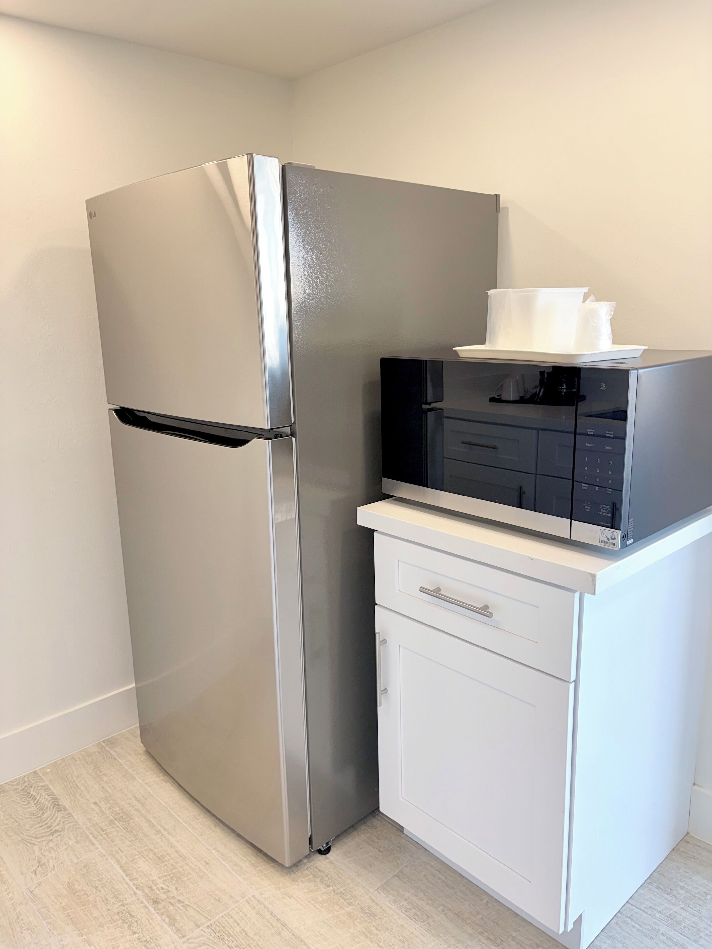 A compact kitchen with a stainless steel refrigerator, a built-in microwave, and a small white cabinet with drawers.