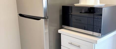 A compact kitchen with a stainless steel refrigerator, a built-in microwave, and a small white cabinet with drawers.
