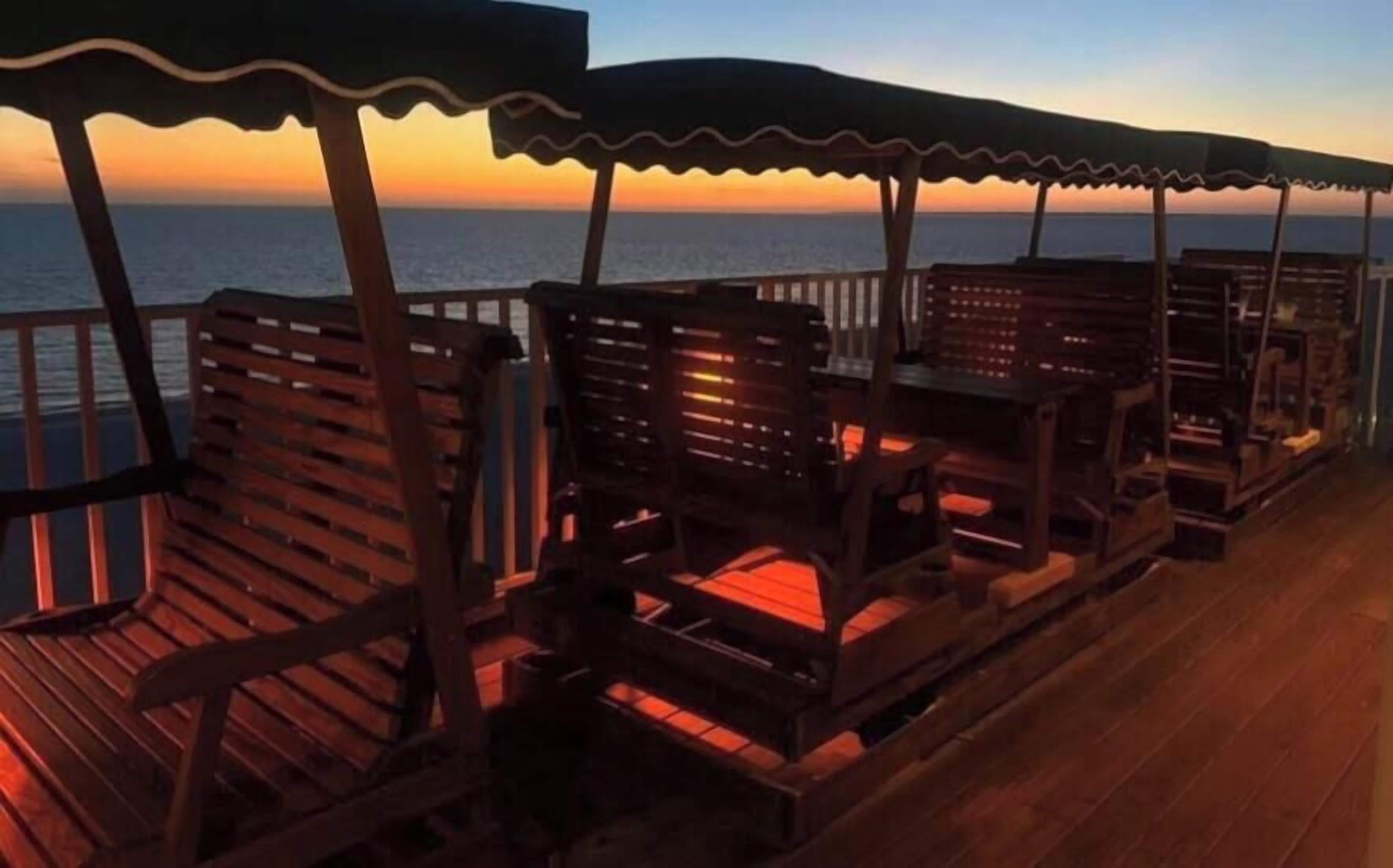 A wooden deck with benches and umbrellas, overlooking the sea during sunset.