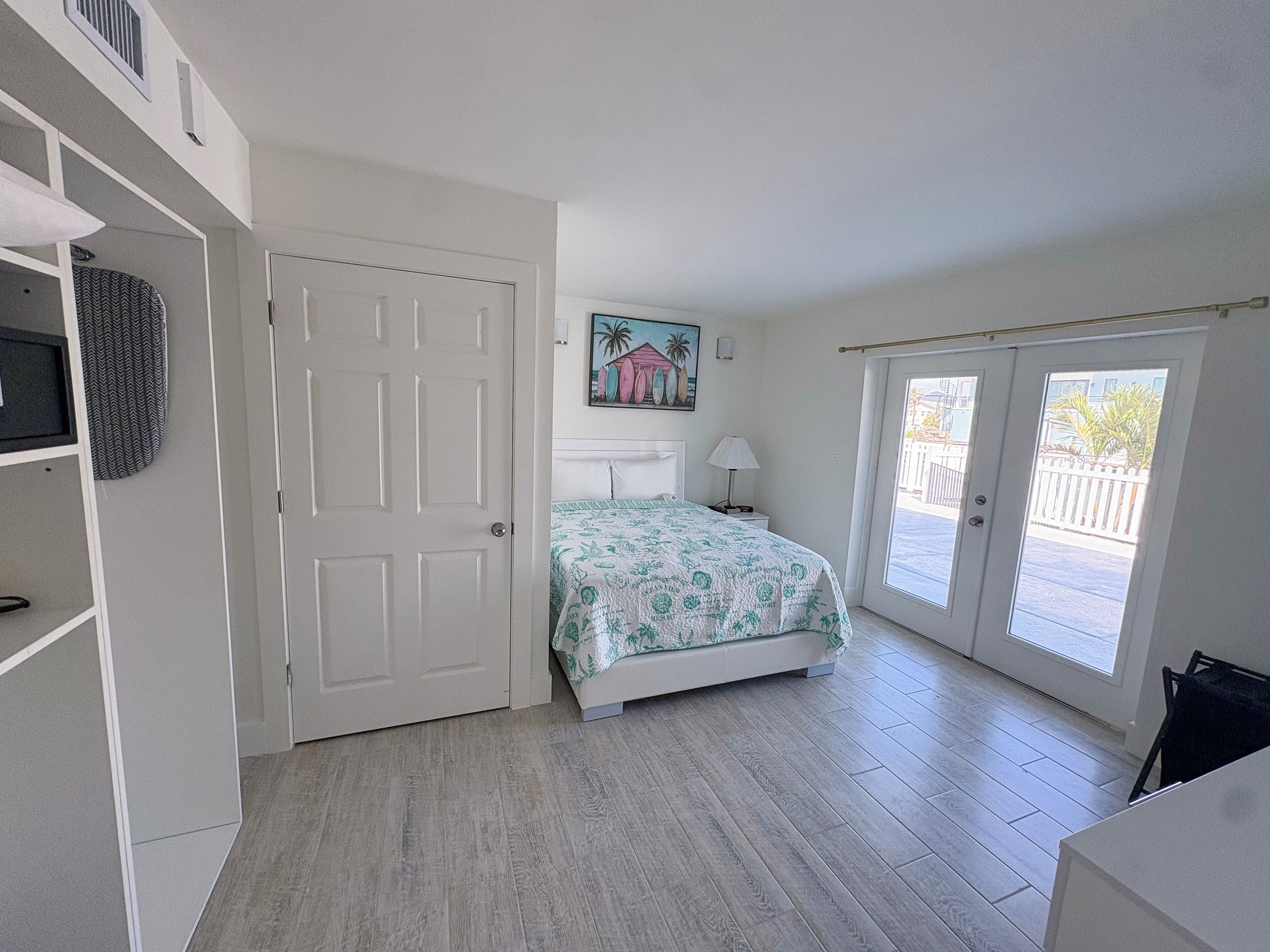 A bedroom with a bed, a door, a window, and a painting on the wall.