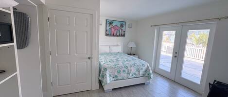 Un dormitorio con cama, puerta, ventana y un cuadro en la pared.