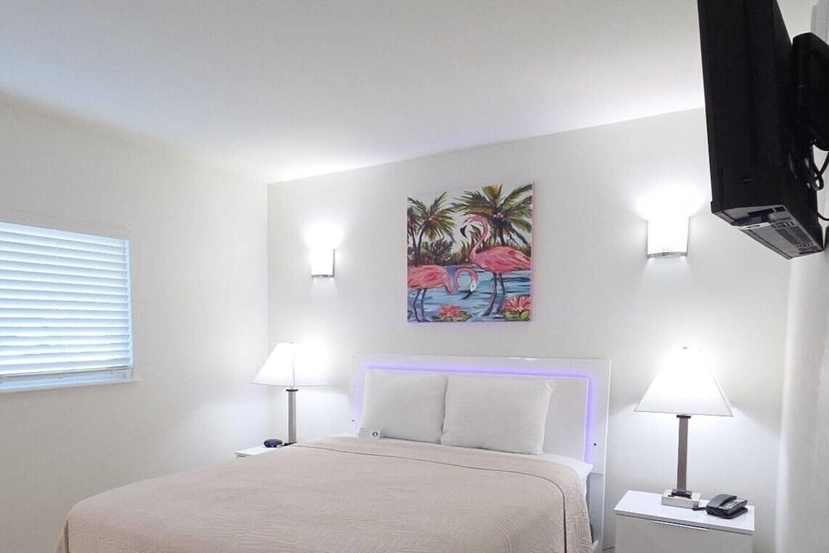 A bedroom with a bed, bedside tables, a painting, and a TV mounted on the wall.