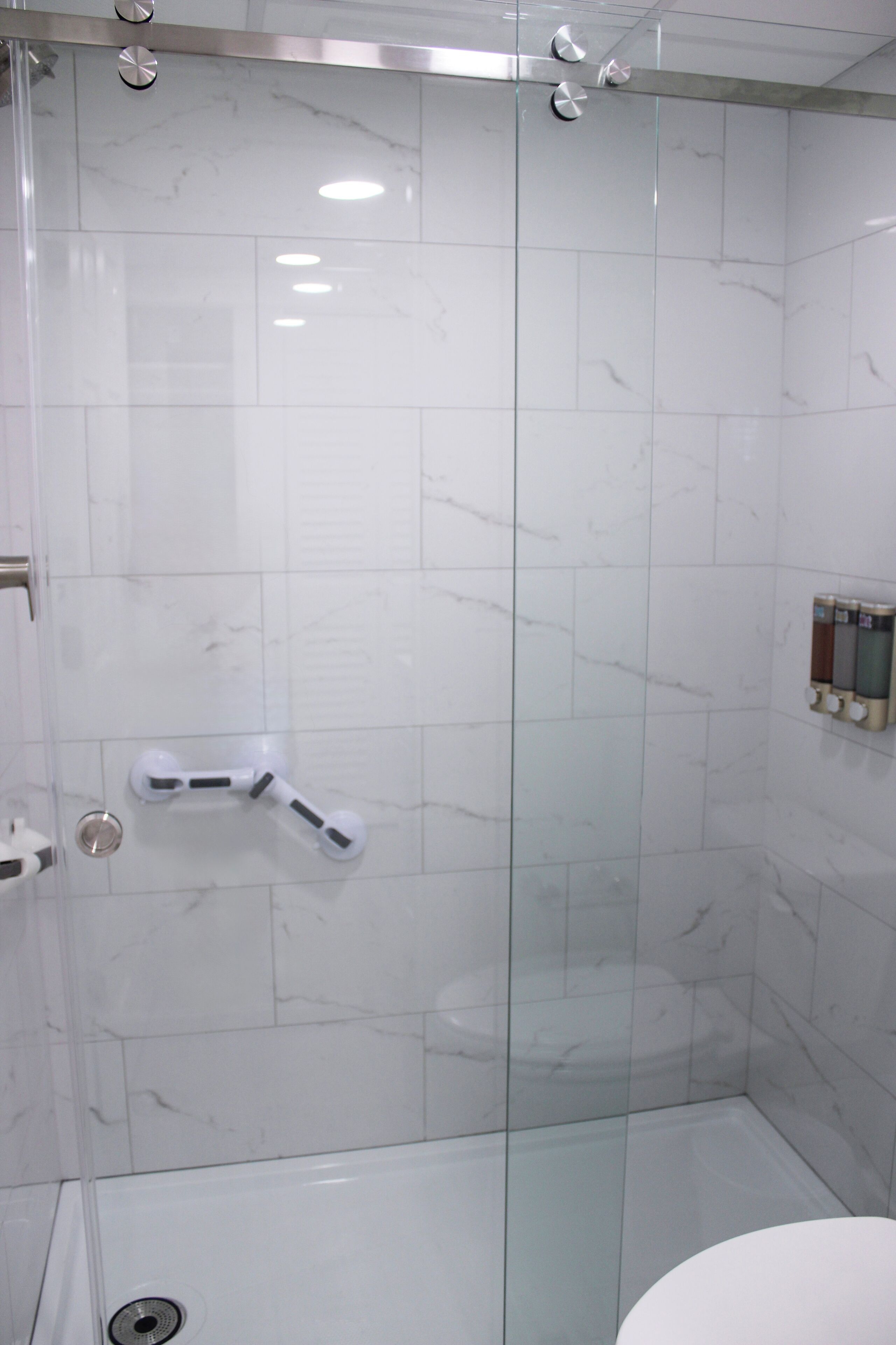 A modern bathroom with a glass shower enclosure, white marble tiles, and a toilet with a bidet attachment.