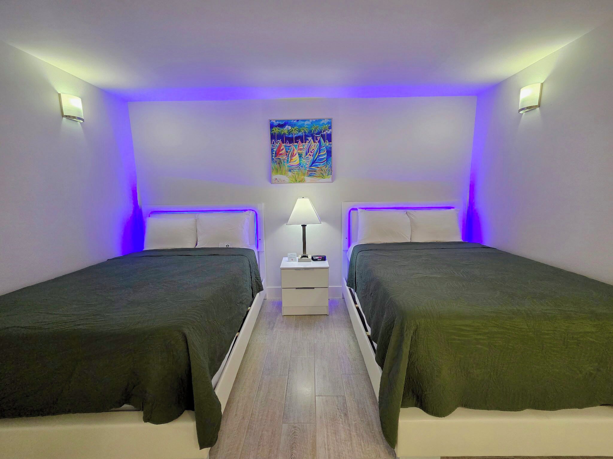 A room with two beds, a nightstand, a lamp, and a painting on the wall.