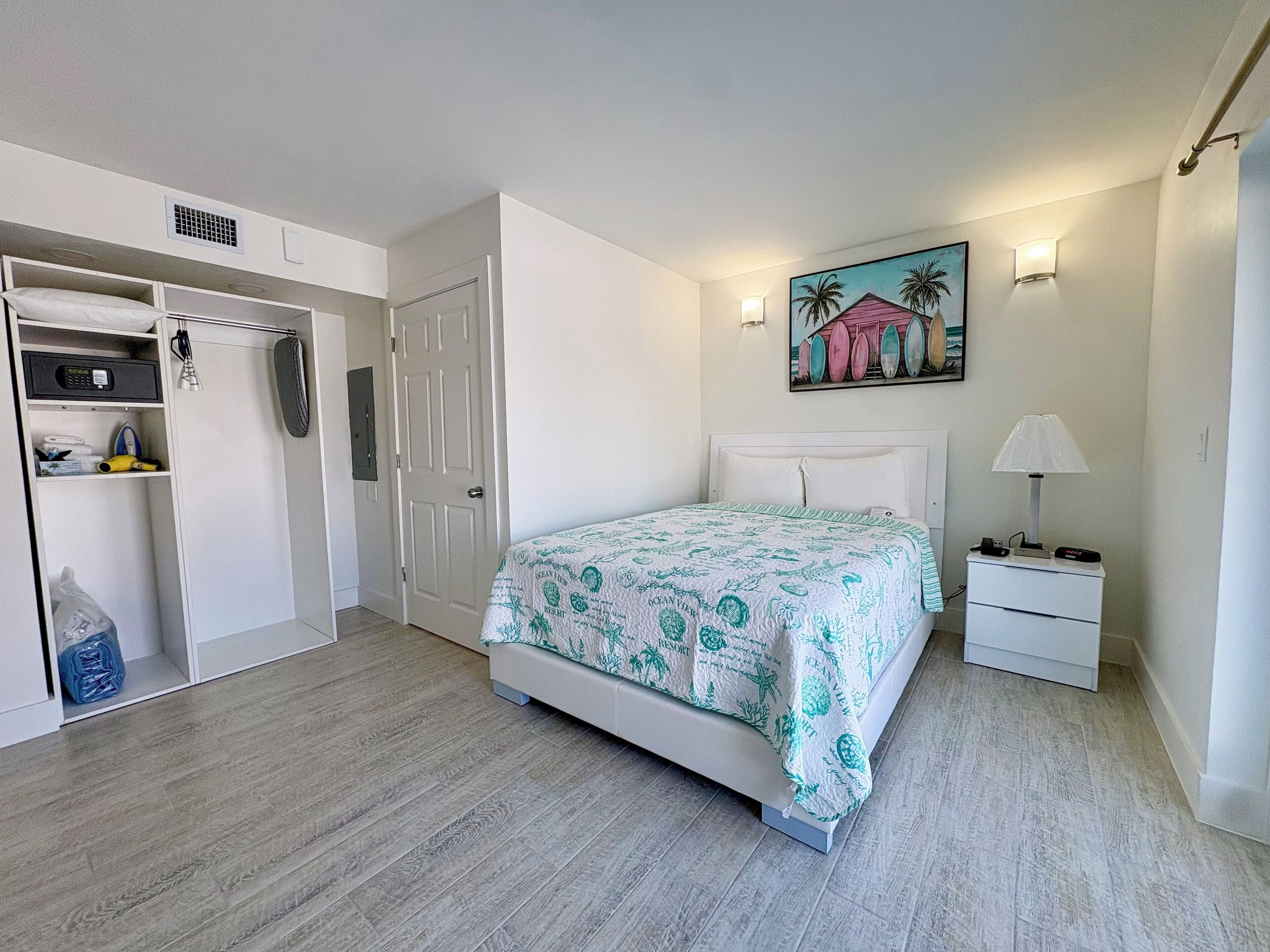 A bedroom with a bed, a nightstand, a lamp, a painting, and a wardrobe.