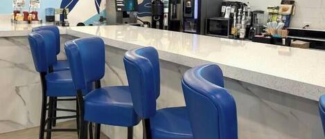 A cafe interior with a counter, bar stools, and a neon sign.