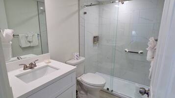 Een moderne badkamer met een douche met glazen wand, een witte wastafel en een toilet.
