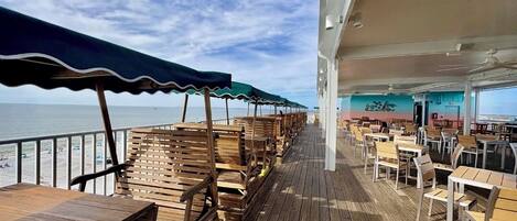 A deck with wooden tables and chairs, a railing overlooking the sea, and a sign indicating the location at Lani Kai Island Resort.