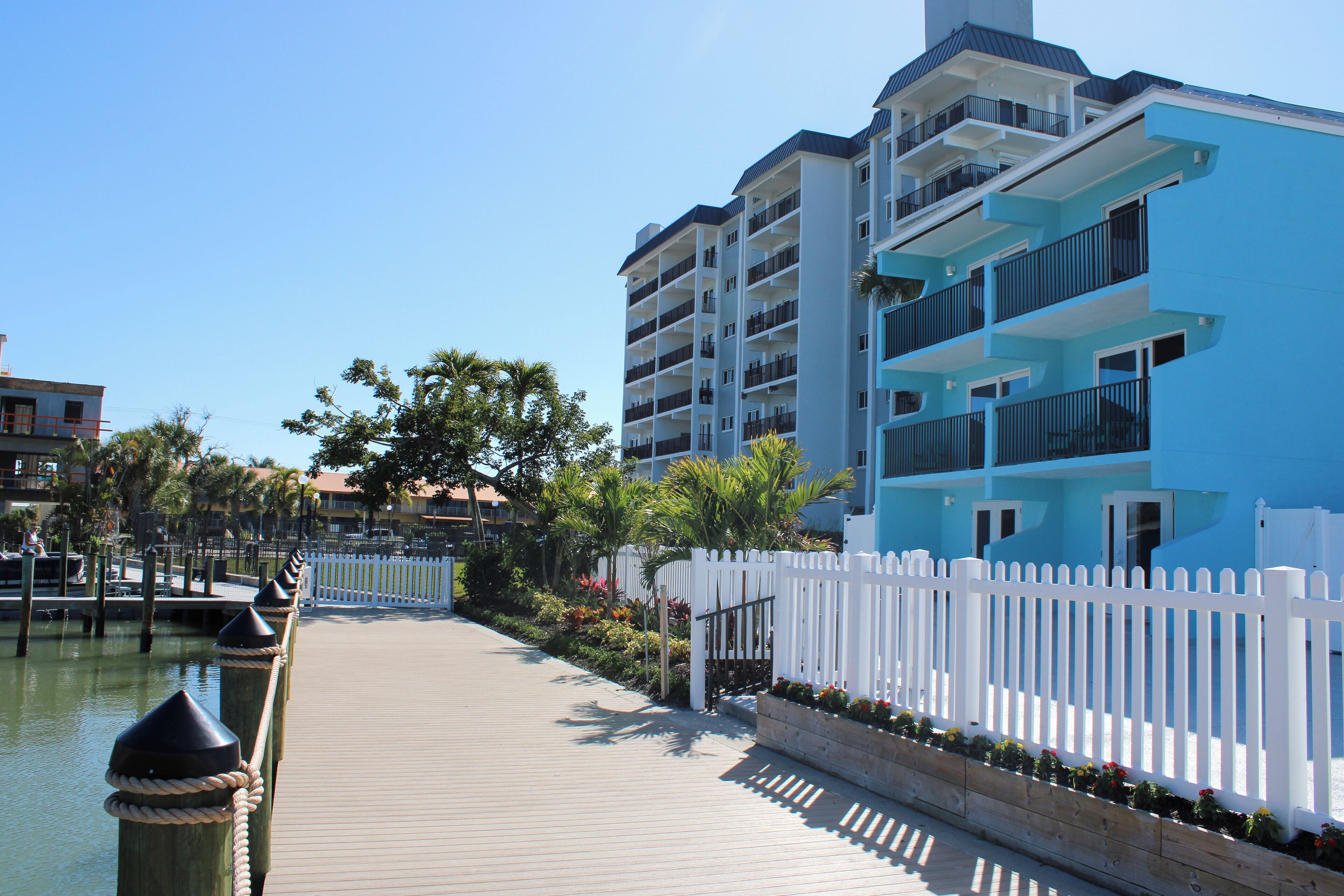 A waterfront hotel with a wooden boardwalk, white picket fence, and balconies overlooking the water.