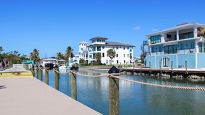 Une propriété située au bord de l’eau, dotée d’un quai, d’un grand bâtiment avec de nombreux balcons et surplombant un ciel d’un bleu éclatant.