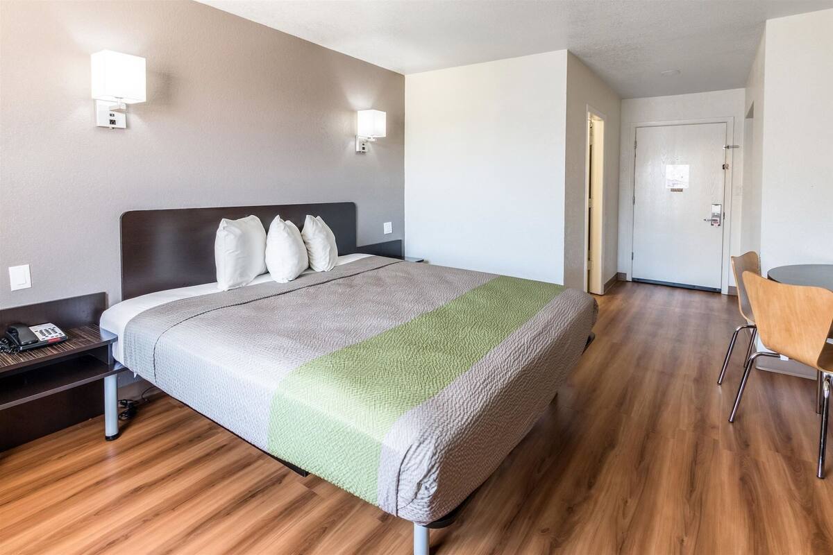 A hotel room with a bed, bedside table, lamp, and a chair.