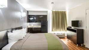 Una habitación de hotel compacta con cama, kitchenette pequeño, televisor y escritorio.