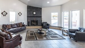 Un salón espacioso con chimenea, sofás de cuero y ventanas amplias que ofrecen vistas al exterior.
