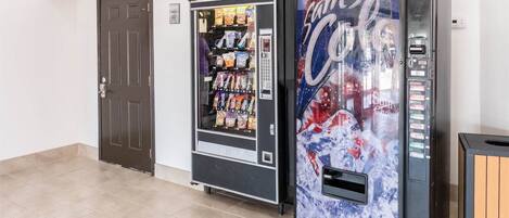 Un distributeur automatique orné d’une publicité pour Coca-Cola, avec une porte à côté.