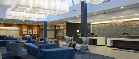 A modern lobby with a reception desk, seating area with sofas and chairs, and a unique ceiling design.